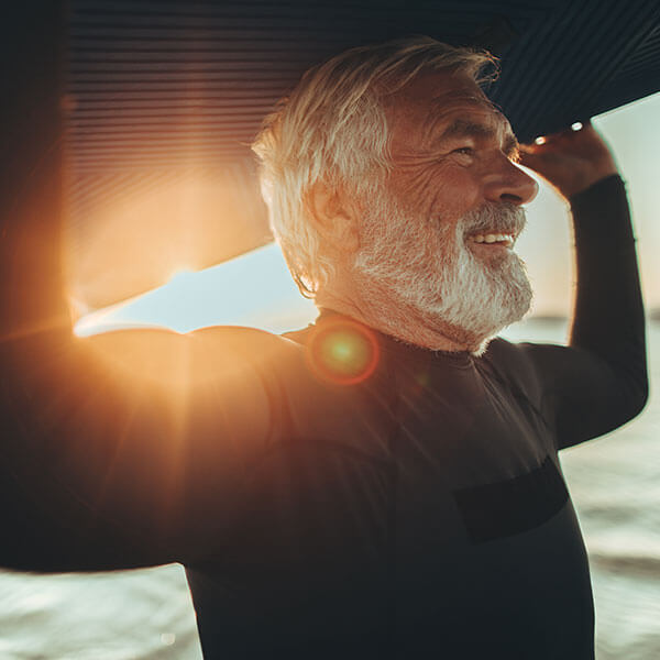 elderly man holding surf board over head