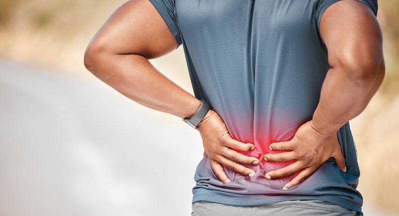 Person holding lower back due to back pain and discomfort in Houston & Texas
