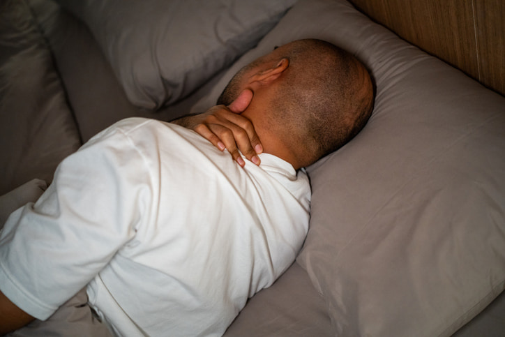 Person sleeping in bed with hand placed on neck for support in Houston & Texas