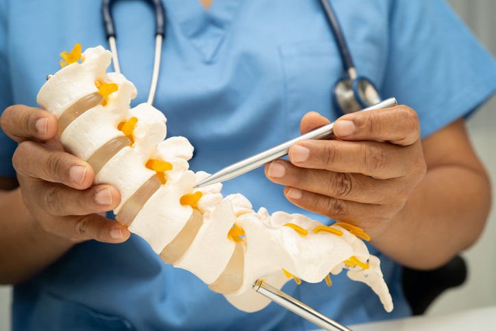 A medical professional explaining spinal fusion surgery with a spine model in Houston & Texas